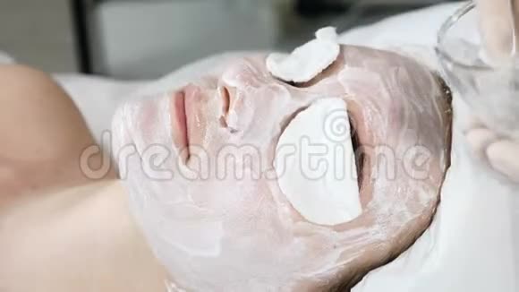 医疗诊所年轻迷人的女人得到专业的面部护理美容师将面霜面膜贴在脸上视频的预览图