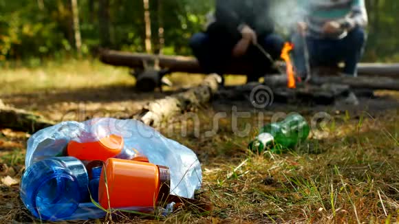 一个装有塑料垃圾的包裹躺在一片空地上燃烧着火焰人们在后台散步野营和大自然视频的预览图