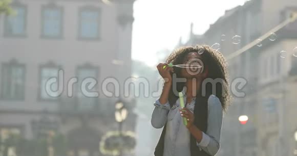 那位穿着时髦的微笑着的美国黑人女孩的肖像吹着肥皂泡在里面旋转视频的预览图