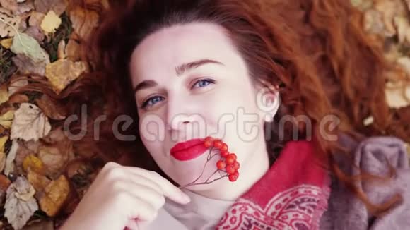 美丽的红发女孩躺在干燥的叶子上微笑着在秋天的森林里放松慢动作3840x21604k视频的预览图