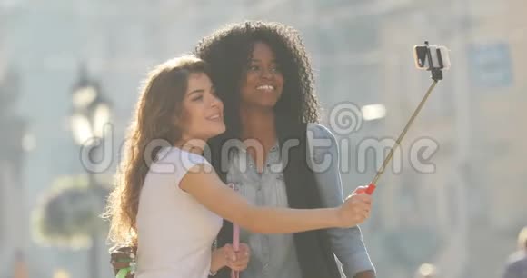 两个好玩的多元文化女朋友在用自拍棒拍照时跳着街道视频的预览图
