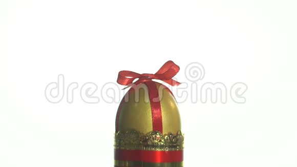 一个金色的鸡蛋白色背景的玻璃杯里放着红色的丝带视频的预览图