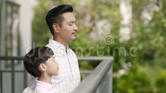 亚洲父子站在阳台上微笑着互相看着深呼吸视频的预览图