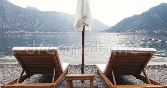 两张带太阳伞的躺椅在被群山环绕的海边避暑山庄浪漫度假视频的预览图