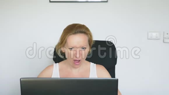 一个女人用她的笔记本电脑坐在桌子旁愤怒和愤怒发誓人类的情感网络成瘾的概念视频的预览图