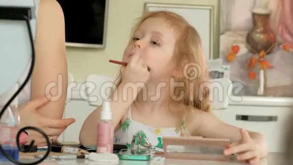 小女孩看着她的母亲在家里做好准备玩她的化妆视频的预览图