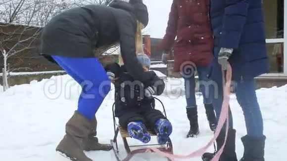 一家人在后院用雪橇骑着快乐的学步男孩的慢动作视频视频的预览图