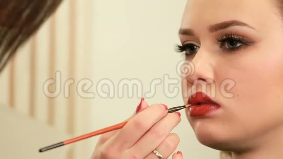 化妆师为美丽的年轻女性特写的嘴唇作画视频的预览图