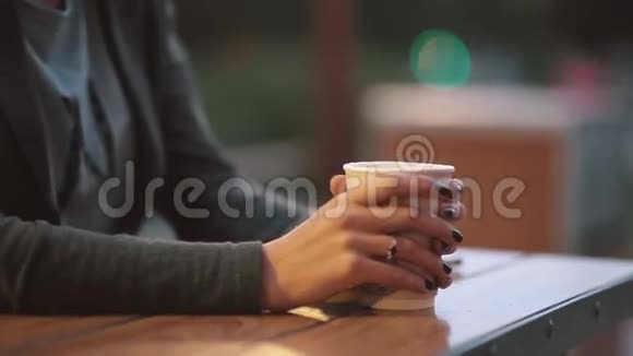 特写女人的手拿着一杯咖啡从茶杯里冒出油烟模糊的灯光城市街道视频的预览图