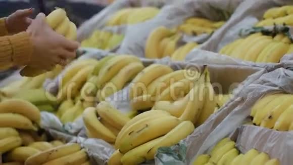 特写镜头看到年轻女子的手在超市里挑选香蕉拿着一些展示水果4K视频的预览图
