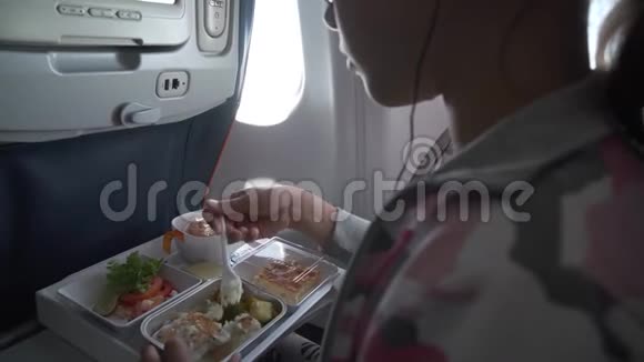 戴着耳机的年轻女孩正在飞机上吃美味的晚餐视频的预览图