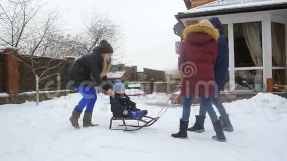在后院和家人一起坐在雪橇上的可爱微笑的小男孩慢镜头视频的预览图