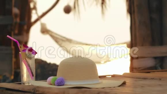 背景沙滩吊床上的女式夏帽和清爽鸡尾酒杯视频的预览图