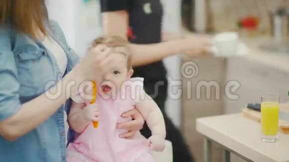 可爱的小女孩坐在妈妈腿上把刷子塞进嘴里视频的预览图