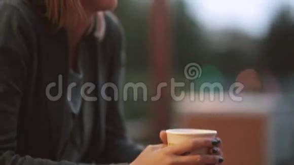 特写女人的手拿着一杯咖啡镜头移向女孩的笑脸模糊的灯光背景视频的预览图