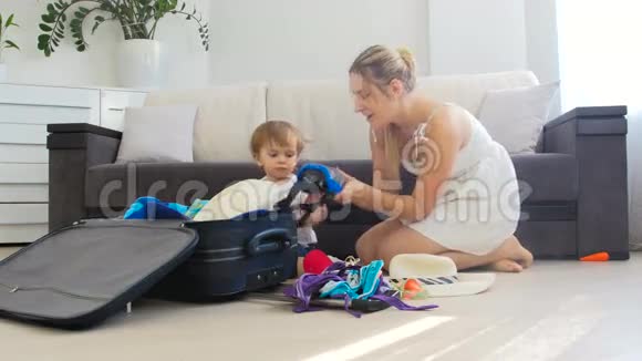 可爱的幼儿男孩带着妈妈在客厅的地板上打包旅行箱度假视频的预览图