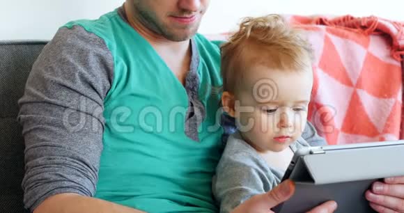 父亲带着他的小男孩在4k客厅用数码平板电脑视频的预览图