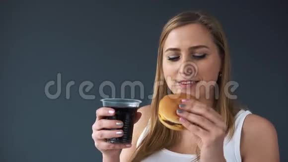 超重的女人在灰色背景下吃汉堡包喝汽水摄像机向下移动显示视频的预览图
