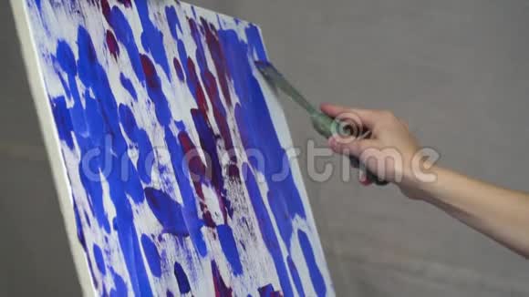 一个女人用金属刮刀在画布上涂抹彩色的慢动作拍摄视频的预览图