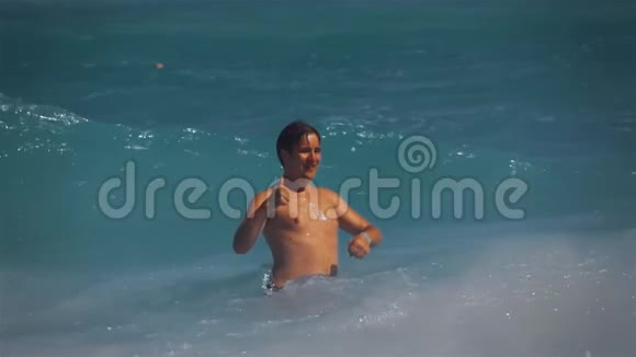 站在海洋里的年轻人用大拇指击打海浪视频的预览图