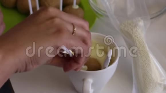一个女人把饼坯浸入融化的白巧克力中将釉面均匀展开附近有其他烹饪原料视频的预览图