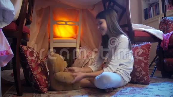 多莉拍了一张可爱的笑脸女孩穿着睡衣在用毯子做的房子里和泰迪熊玩耍视频的预览图