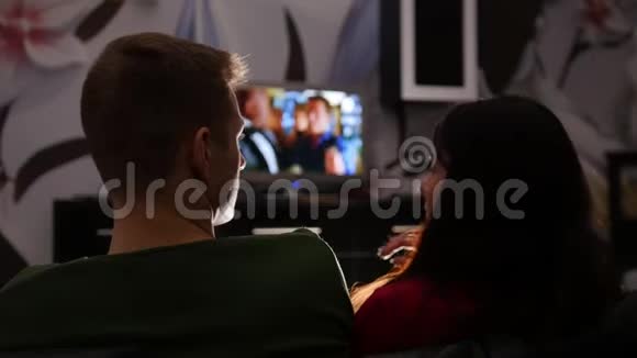 年轻可爱的夫妇坐在沙发上看电视视频的预览图