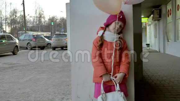 早春一个小女孩带着五颜六色的气球走在城里的一条街上视频的预览图