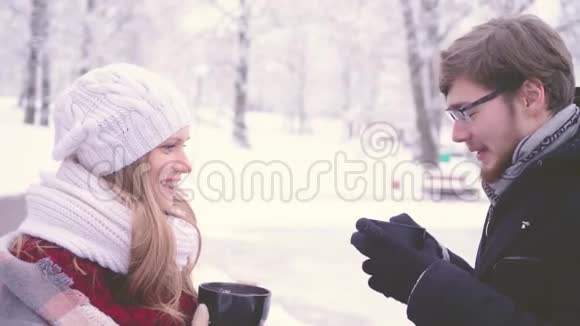 在冬天的公园里美丽的女孩和长胡子的男人一边说一边喝着杯子里的热可可一边笑视频的预览图
