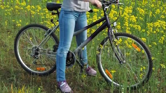 油菜田带着自行车的女孩在田野里开着黄色的花骑自行车的女孩正把胳膊伸过自行车视频的预览图
