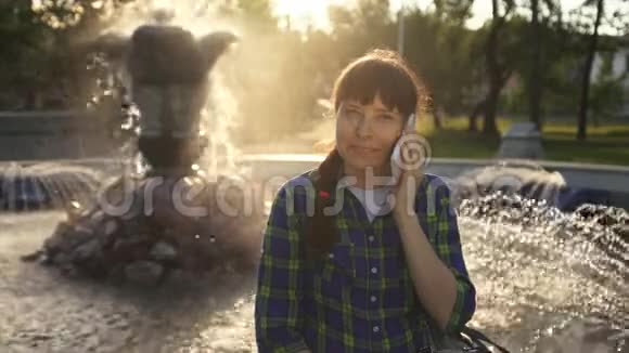 日落时分一个女人在喷泉附近使用白色智能手机视频的预览图