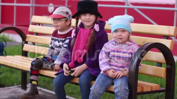 三个快乐的孩子坐在木凳上挥手视频的预览图
