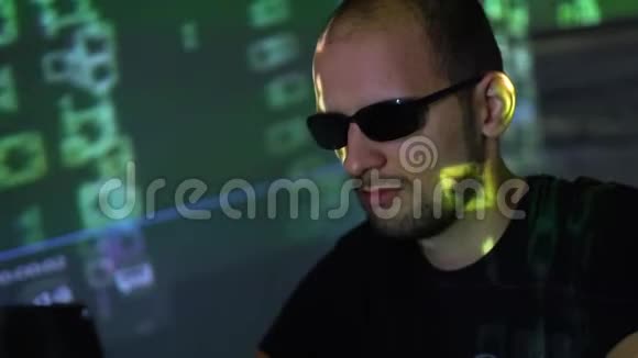 一个戴太阳镜的黑客在黑暗的房间里使用程序代码视频的预览图
