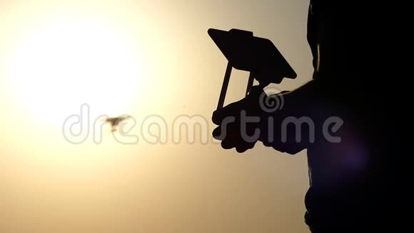 一只雄性手的特写控制面板和日落时的飞行无人机视频的预览图