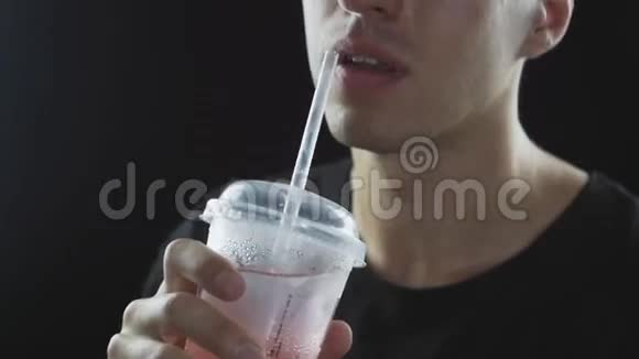 男人通过吸管从快餐中喝柠檬水隔离在黑色的背景上视频的预览图