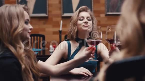 三个穿着鸡尾酒礼服的迷人女人欢呼着喝着红酒用老式的方式交谈着视频的预览图