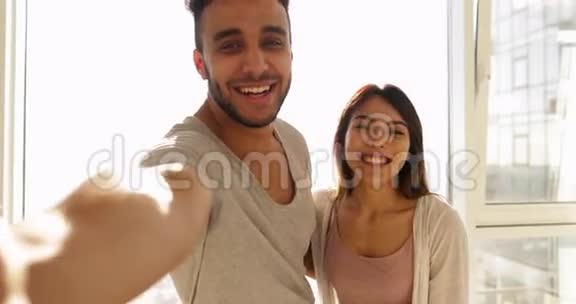 年轻的混血情侣在大窗晨曦上自拍快乐的西班牙男人亚洲女人拥抱视频的预览图