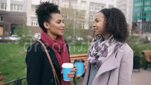 两个漂亮的混血女人带着购物袋喝着咖啡在街上说话年轻女孩微笑着视频的预览图