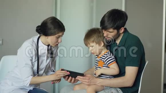 年轻的女医生和小男孩的父亲在医疗办公室用平板电脑交谈视频的预览图