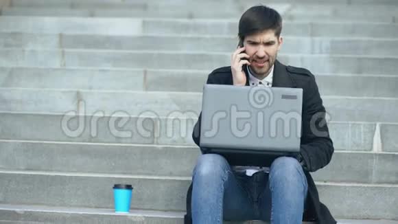 年轻的商人带着笔记本电脑打电话后有压力坐在街上的楼梯上商人视频的预览图
