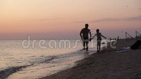 父亲和儿子在日落时在海滩上玩耍友好家庭观念视频的预览图