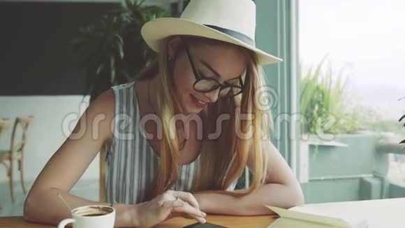 年轻女性在咖啡馆做智能手机女人在手机上使用应用程序微笑和日光浴视频的预览图