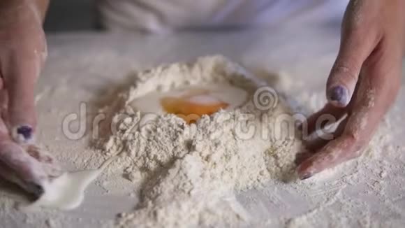 女性手在厨房表面将面粉与鸡蛋和牛奶混合的特写镜头慢镜头视频的预览图