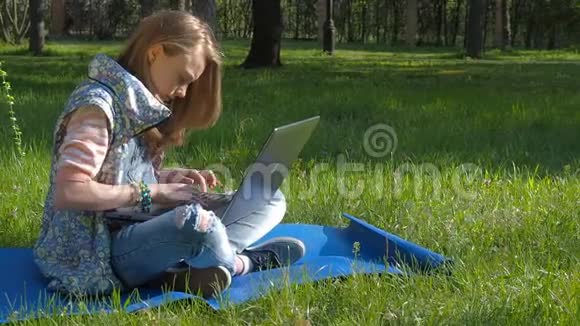女孩在瑜伽姿势与笔记本电脑大自然中的一个十几岁的女孩正在笔记本电脑上打字一个穿着牛仔裤和手镯的少年视频的预览图