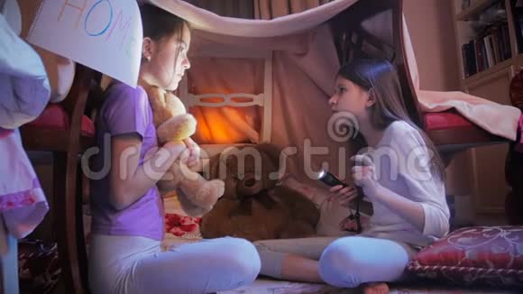 两个穿着睡衣的十几岁女孩坐在卧室的地板上用手电筒讲恐怖的故事视频的预览图