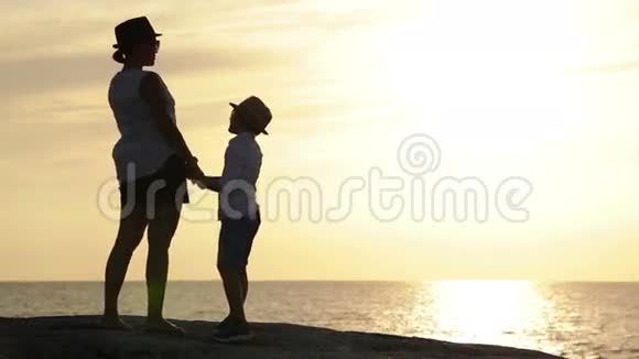 母亲和儿子呆在露头上日落时俯瞰大海笑了起来视频的预览图
