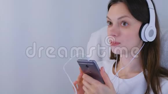 女人在智能手机上用耳机听音乐唱一首歌视频的预览图