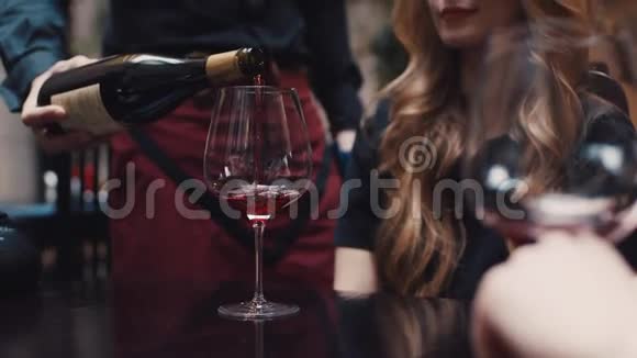 一个服务员把红酒倒在杯子里为一个有着优雅发型的迷人的年轻女人玩得开心视频的预览图