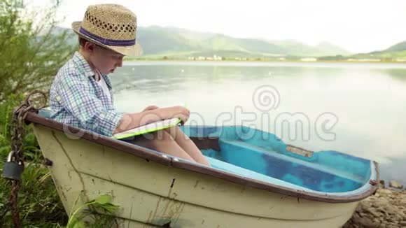 一个男孩坐在停泊在岸边的木船上看书视频的预览图