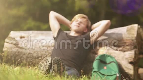 年轻的旅行者在阳光下的大树茎上休息视频的预览图